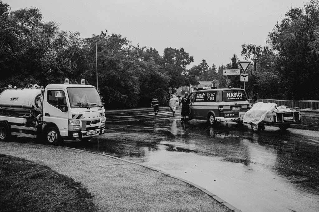 Services Black and white image of emergency vehicles on a rainy street with first responders.